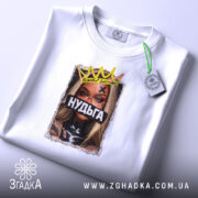 Футболка Нудьга корона, біла, на столі, ракурс зверху, фон світло-сірий, принт з зображенням жінки з короною та написом 'Нудьга' на чорному фоні, з біркою.