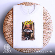 Футболка Нудьга корона, біла, на столі, ракурс зверху, фон плетений, принт з зображенням жінки з короною та написом 'Нудьга' на чорному фоні.