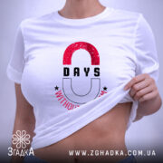 Футболка Нуль днів без сарказму, біла, на столі, з етикеткою, фон світло-сірий, принт з червоними і чорними літерами, напис '0 DAYS WITHOUT SARCASM' з зірочками.