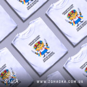 Футболка образити може кожен. Біла футболка на моделі, зображена з правого ракурсу. Фон світло-фіолетовий. Принт з ілюстрацією дівчинки в українському вбранні з квітковим вінком на голові, тримає ножі, текст зверху і знизу принта чорного кольору.