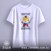 Футболка образити може кожен. На фото зображена біла футболка, підвішена на вішалці. Принт з мультяшним персонажем, який тримає два мечі, розташований в центрі. Фон світло-сірий, що підкреслює простоту дизайну футболки.