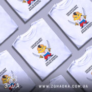 Футболка образити може кожен. На фото зображена біла футболка, зображення розташоване в центрі. Принт з мультяшним персонажем, який тримає два мечі, виконаний у яскравих кольорах. Фон світло-фіолетовий, що підкреслює яскравість принта.