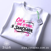 Футболка ой я не пʼяна, на фото зображена складена біла футболка, принт на ній яскравий, текст виконаний у чорному та рожевому кольорах, фон світло-сірий, на футболці є етикетка.