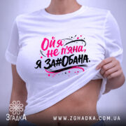 Футболка ой я не пʼяна, на фото зображена складена біла футболка, принт на ній яскравий, текст виконаний у чорному та рожевому кольорах, фон світло-сірий, на футболці є етикетка.