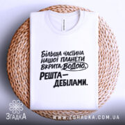 Футболка планета вкрита водою, біла футболка на плетеній основі, ракурс зверху, фон світлий, принт чорного кольору з текстом: 'Більша частина нашої планети вкрита водою. Решта – дебілами.'