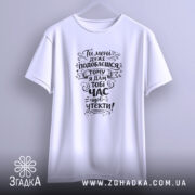 Футболка подобаєшся але біжи швидше. Біла футболка з коротким рукавом, зображена з фронтального ракурсу на світло-фіолетовому фоні. Принт чорного кольору з текстом, оформлений у стилі рукописного шрифту.