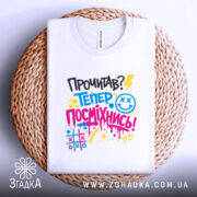 Футболка посміхнись. Біла футболка, складена на плетеній основі, фон світлий. Принт з текстом 'Прочитав? Тепер посміхнись!' у яскравих кольорах, з елементами графіки, добре помітний.