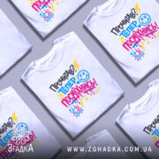 Футболка посміхнись. Біла футболка на молодій людині, зображена в анфас, фон світло-сірий. Принт містить текст 'Прочитав? Тепер посміхнись!' у яскравих кольорах: жовтому, блакитному, рожевому та чорному, з елементами графіки.