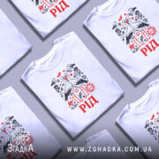 Футболка рід білого кольору, зображена на молодому чоловікові, який позує на світло-фіолетовому фоні. Принт на футболці містить двох лелек, що цілуються, оточених рослинними мотивами, червоним написом 'РІД' та сонцем. Рукава футболки злегка закочені.