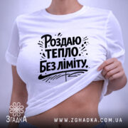 Футболка роздаю тепло без ліміту, біла, з верхнього ракурсу, на плоскій поверхні, фон світло-сірий, принт чорного кольору з написом 'Роздаю тепло без ліміту' та елементами дизайну, з етикеткою зеленого кольору.