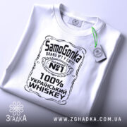 Футболка самогонка, біла, на столі, з верхнього ракурсу, фон світло-сірий, принт чорного кольору з написом 'SamoGonka', '100% УКРАЇНСЬКИЙ WHISKEY' та етикеткою з зеленим шнурком.