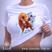 Футболка самурайська білка, біла, на столі, ракурс зверху, фон світло-фіолетовий, принт з зображенням білки-самурая, на футболці є етикетка з логотипом.