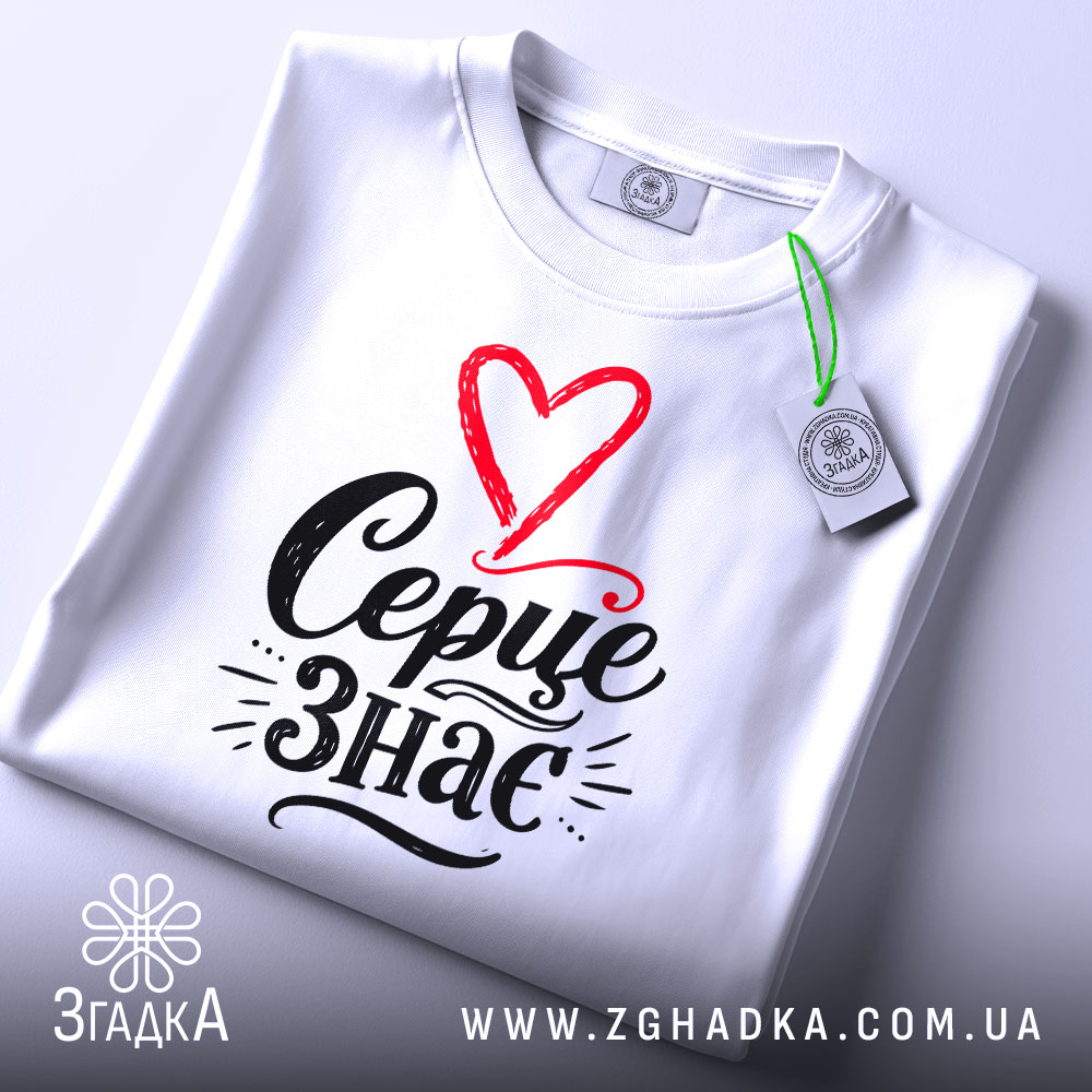 Футболка Серце знає, біла, зображена на плоскій поверхні, фон світлий, принт з червоним серцем і чорним написом 'Серце знає', видна етикетка з логотипом.