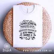 Футболка сміх і секс продовжують життя, біла, зображена зверху на плетеній основі, ракурс зверху, фон світло-фіолетовий, принт чорного кольору з текстом і декоративними елементами.