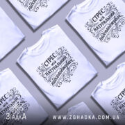 Футболка Стрес мій підсолоджувач, біла, на моделі, з легким ракурсом спереду, фон світло-фіолетовий, принт чорного кольору з витонченими декоративними елементами.