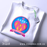 Футболка супер мама, біла, з плоским ракурсом, фон світло-сірий, принт з написом 'СУПЕР' та серцем, кольори принта: рожевий, жовтий, блакитний, з етикеткою на комірці.