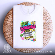 Футболка світ божеволіє, біла, складена на плоскій поверхні, фон світло-сірий, принт яскравий з текстом і графічними елементами в кольорах: рожевий, зелений, жовтий, чорний, з малюнками грошових купюр, динамічними лініями та вогнем.