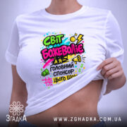 Футболка світ божеволіє, біла, на плоскій поверхні, з принтом в центрі, фон світло-сірий, принт яскравий з текстом і графічними елементами в кольорах: рожевий, зелений, жовтий, чорний, з малюнками грошових купюр, динамічними лініями та вогнем.