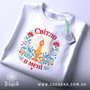 Футболка Світло в мені, біла, на столі, з принтом свічки та квітів, фон світло-сірий, деталі принта яскраві, з червоними, жовтими та зеленими елементами, з етикеткою.