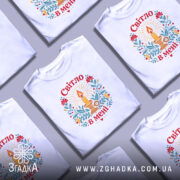 Футболка Світло в мені, біла, на моделі, з принтом свічки та квітів, фон світло-сірий, деталі принта яскраві, з червоними, жовтими та зеленими елементами.