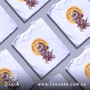 Футболка свобода дорожча, біла футболка на чоловіку, зображення принта з воїном та птахом, фон світло-сірий, принт у коричневих та жовтих тонах.