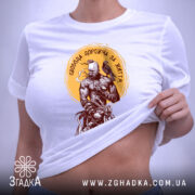 Футболка свобода дорожча, складена біла футболка з принтом, вид зверху, фон світло-сірий, принт з воїном та птахом, етикетка з зеленим шнурком.