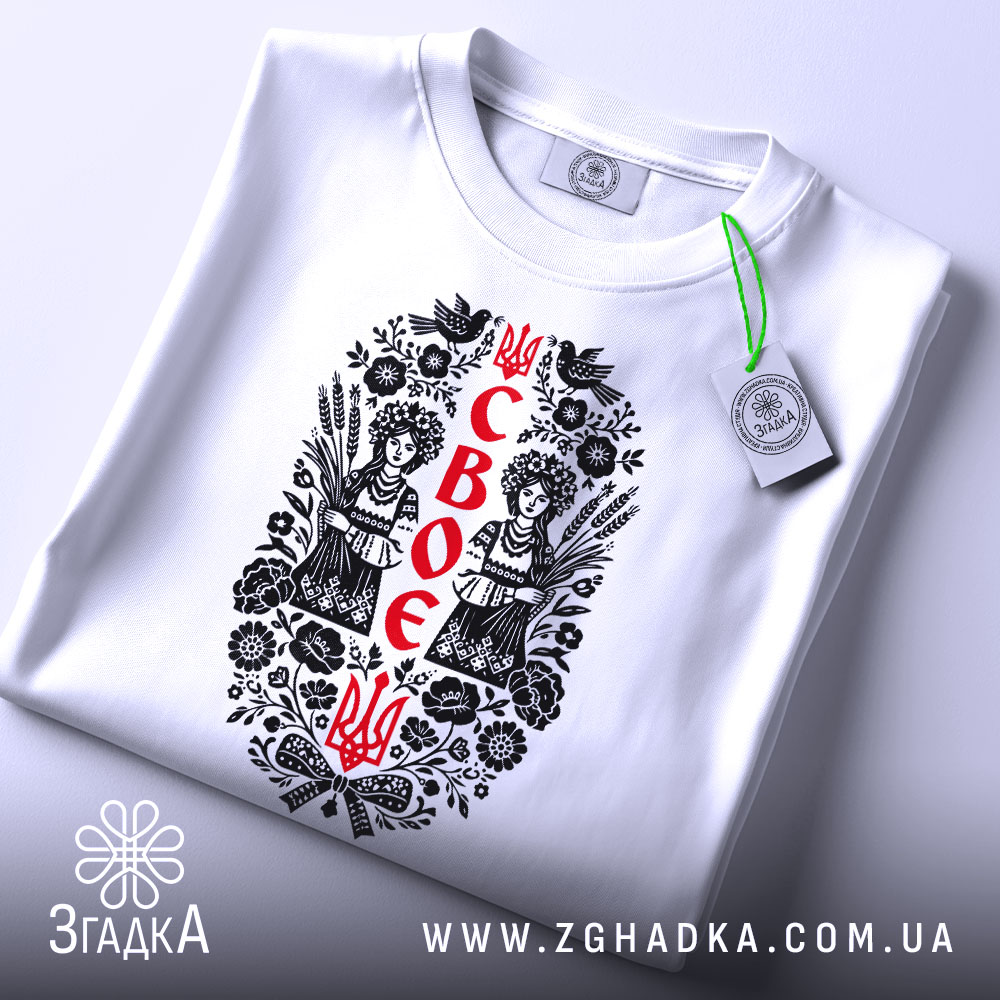 Футболка своє українське, біла, на плоскій поверхні, з принтом у центрі, що зображує двох дівчат у національному вбранні, оточених рослинними мотивами, з зеленим ярликом.