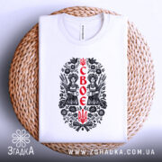 Футболка своє українське, біла, на плоскій поверхні, з принтом у центрі, що зображує двох дівчат у національному вбранні, оточених рослинними мотивами, на плетеній основі.