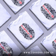 Футболка своє українське, біла, на моделі, з принтом у вигляді двох дівчат у національному вбранні, оточених квітами та символікою України, фон світло-фіолетовий.