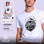 Футболка Сила Карпат, біла, на моделі, з легким ракурсом спереду, фон світло-фіолетовий, принт чорного кольору з горами та написом 'Сила Карпат у моїх жилах'.