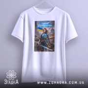 Футболка сильна українська жінка, біла, підвішена на вішалці, з фронтальним ракурсом, фон світлий, принт з героїнею в броні з мечем, на фоні зруйнованого міста та українським прапором.