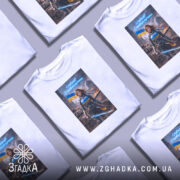 Футболка сильна українська жінка, біла, зображена на моделі з легким ракурсом спереду, фон світлий, принт з героїнею в броні з мечем, на фоні зруйнованого міста та українським прапором.
