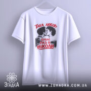 Футболка така любов, біла, підвішена на вішалці, з принтом, що зображує пару, яка цілується, текст червоним кольором: 'ТАКА ЛЮБОВ БУВАЄ РАЗ В НІКОЛИ', фон ніжно-сірий, виглядає стильно.