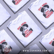 Футболка така любов, біла, на моделі, з принтом, що зображує пару, яка цілується, текст червоним кольором: 'ТАКА ЛЮБОВ БУВАЄ РАЗ В НІКОЛИ', фон ніжно-фіолетовий, стильний і сучасний.