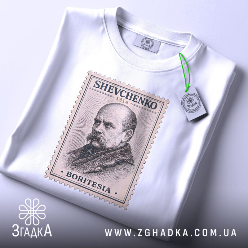 Футболка Тарас Шевченко білого кольору, зображена на плоскій поверхні, ракурс зверху, фон світло-фіолетовий, принт у вигляді поштової марки з портретом Тараса Шевченка, текст на марці: 'SHEVCHENKO 1814', 'BORITESIA', на футболці є етикетка з зеленим шнурком.