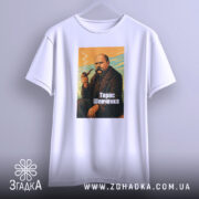Футболка Тарас Шевченко, біла, на вішалці, з ракурсу спереду, фон світло-сірий, принт з зображенням Тараса Шевченка з сигаретою, кольори принта: оранжевий, зелений, чорний, текст "Тарас Шевченко" внизу.