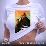 Футболка Тарас Шевченко, біла, на столі, з ракурсу зверху, фон світло-сірий, принт з зображенням Тараса Шевченка з сигаретою, кольори принта: оранжевий, зелений, чорний, текст "Тарас Шевченко" внизу, на футболці є етикетка.