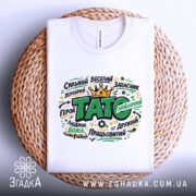 Футболка тато подарунок, біла, на плоскій поверхні, з принтом, що містить слова "ТАТО" та інші позитивні характеристики, фон світлий, деталі принта яскраві, з короною, на плетеній основі.