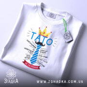 Футболка тато завжди правий, біла, на плоскій поверхні, фон світлий, принт з написом 'ТАТО' у блакитному кольорі, корона жовта, деталі тексту навколо, етикетка на комірці.