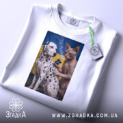 Футболка тату кіт, біла, на столі, з принтом, на якому зображені далматинець і сфінкс на фоні українського прапора, етикетка з зеленим шнурком, деталі принта яскраві.