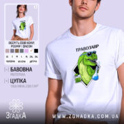 Футболка Травозавр білого кольору, зображена на молодому чоловікові, який позує з легким усмішкою. Принт на футболці зображає зеленого динозавра в окулярах, що тримає колбу з блакитною рідиною та пакет з травою. Фон світло-сірий, а текст 'ТРАВОЗАВР' розташований над принтом.