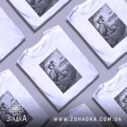 Футболка українські лелеки сімейний символ, біла, на моделі з легким макіяжем, фон світло-фіолетовий, принт з двома лелеками та пташенятами в гнізді, на задньому плані український прапор.