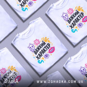 Футболка Важкий характер, біла, зображена на моделі, яка позує з легким усмішкою, фон пастельного кольору, принт складається з кольорових елементів, таких як череп, квіти, очі та зірки, текст "Важкий характер" великими чорними літерами.