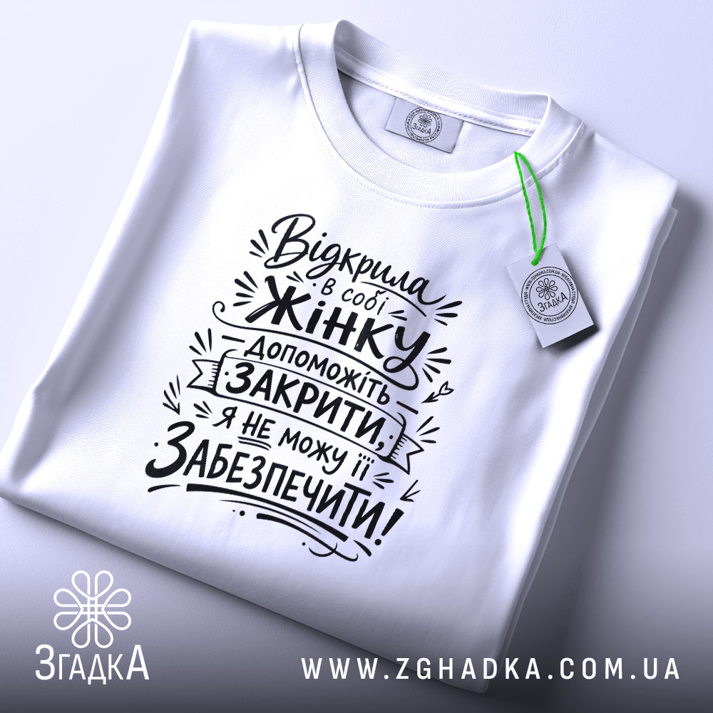 Футболка відкрила в собі жінку, біла футболка, розкладена на поверхні, фон світло-фіолетовий, принт чорного кольору з текстом на тему жіночої підтримки, з етикеткою зеленого кольору.