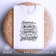 Футболка відкрила в собі жінку, біла футболка, складена на плетеній кошику, фон світло-фіолетовий, принт чорного кольору з текстом на тему жіночої підтримки.