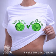 Футболка VIP доступ, біла, складена на столі, фон світлий, принт з двома зеленими капустами та текстом 'VIP доступ ♥ для обранців', видна етикетка з логотипом.