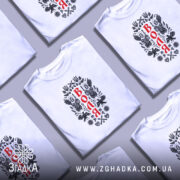 Футболка воля на чоловікові, білого кольору, з принтом на грудях, зображення ангелів та герба України, фон світло-фіолетовий, деталі принта виконані в чорному та червоному кольорах.