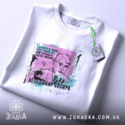 Футболка Володимир Сосюра, біла, зображена на плоскій поверхні, ракурс зверху, фон світло-сірий, принт з портретом Володимира Сосюри з кольоровими акцентами та текстом.