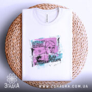 Футболка Володимир Сосюра, біла, складена на плоскій поверхні, ракурс зверху, фон натуральний, текстура плетеного кошика, принт з портретом Володимира Сосюри з кольоровими елементами та текстом.