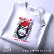 Футболка вулиця мої джунглі, біла, з принтом мавпи в червоній шапці, що курить, на фоні світло-сірого кольору, складена на поверхні, з етикеткою.